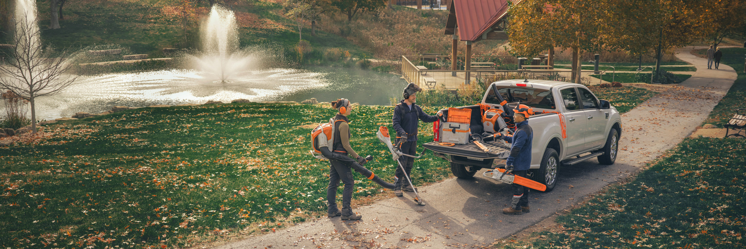  Un grupo de jardineros paisajistas profesionales se encuentran alrededor de sus vehículos y se preparan para su trabajo con máquinas de batería STIHL.