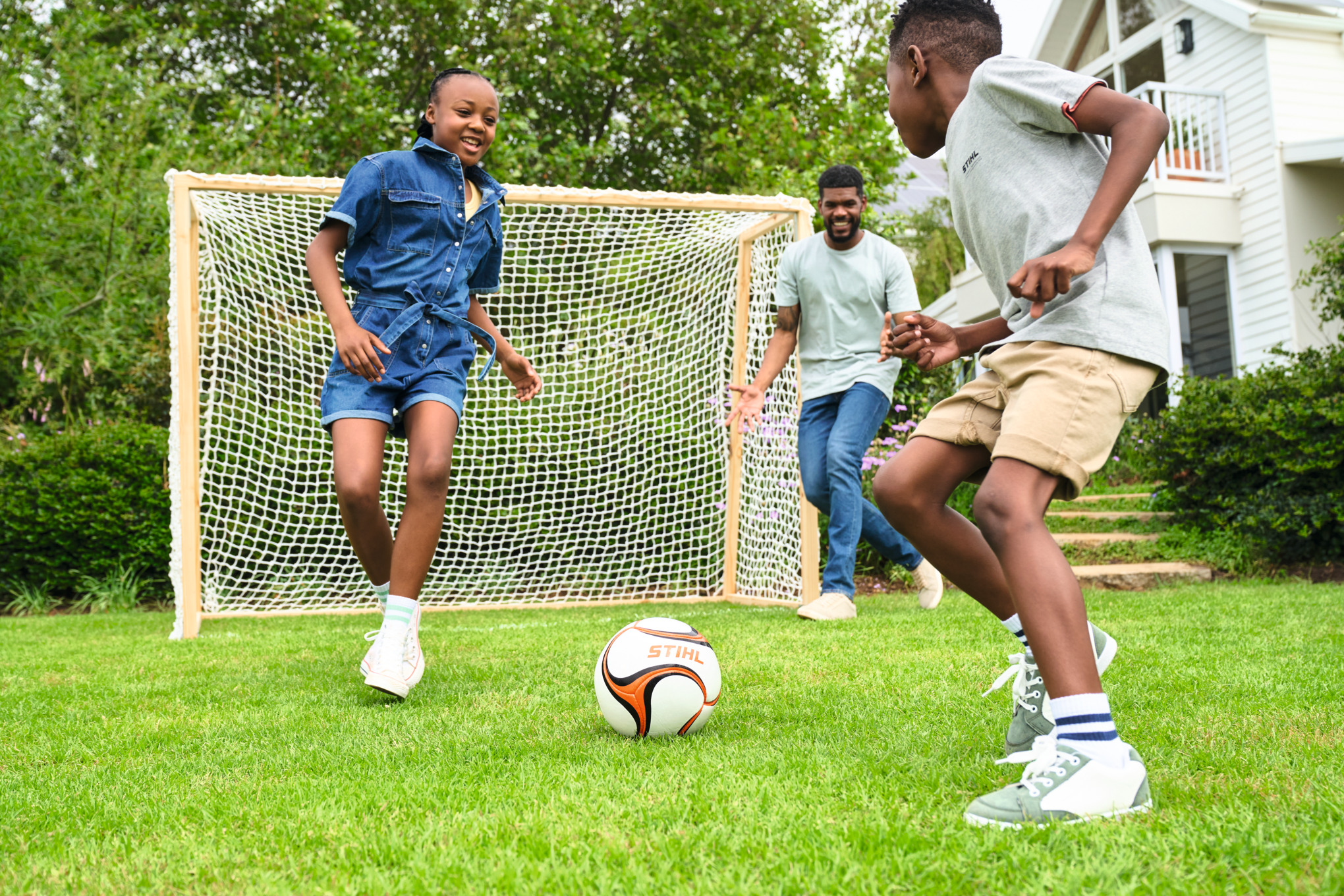Tres niños jugando al fútbol en el jardín con una portería de madera