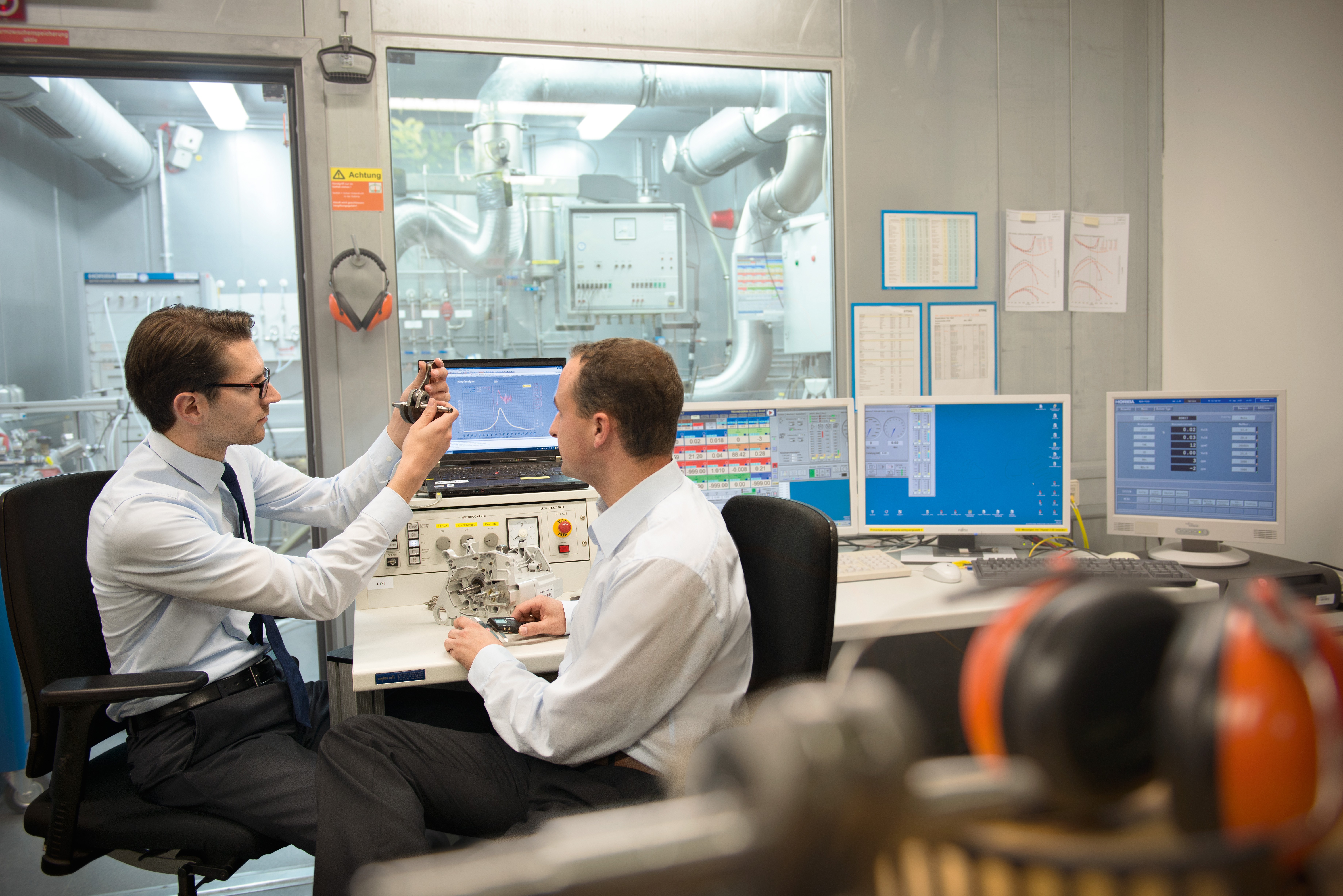 Dos hombres sentados en un laboratorio con varios monitores mientras examinan parte de un nuevo producto