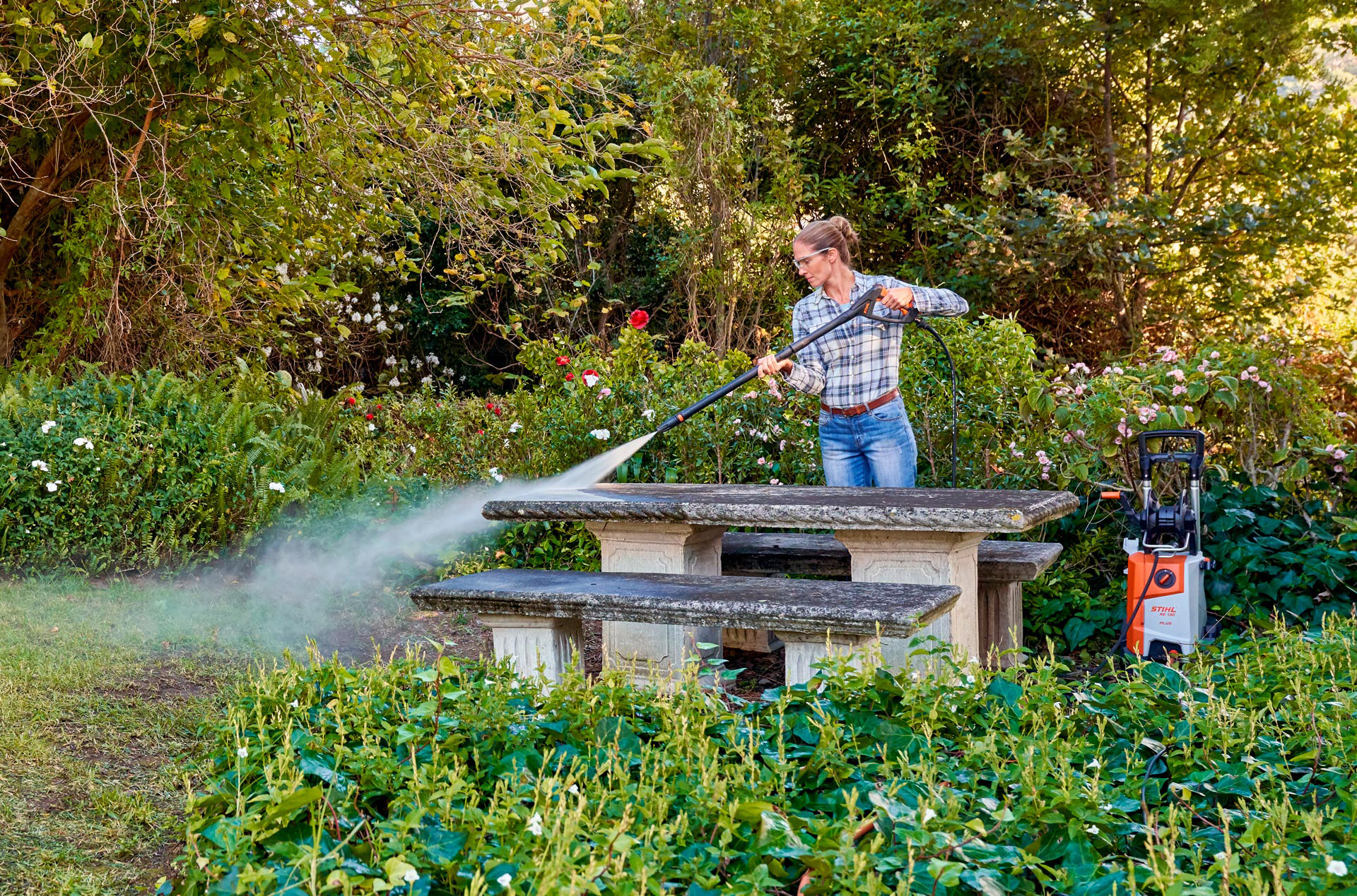 Una mujer hace limpieza de exteriores con una hidrolimpiadora STIHL que echa agua a presión a sus muebles de jardín.
