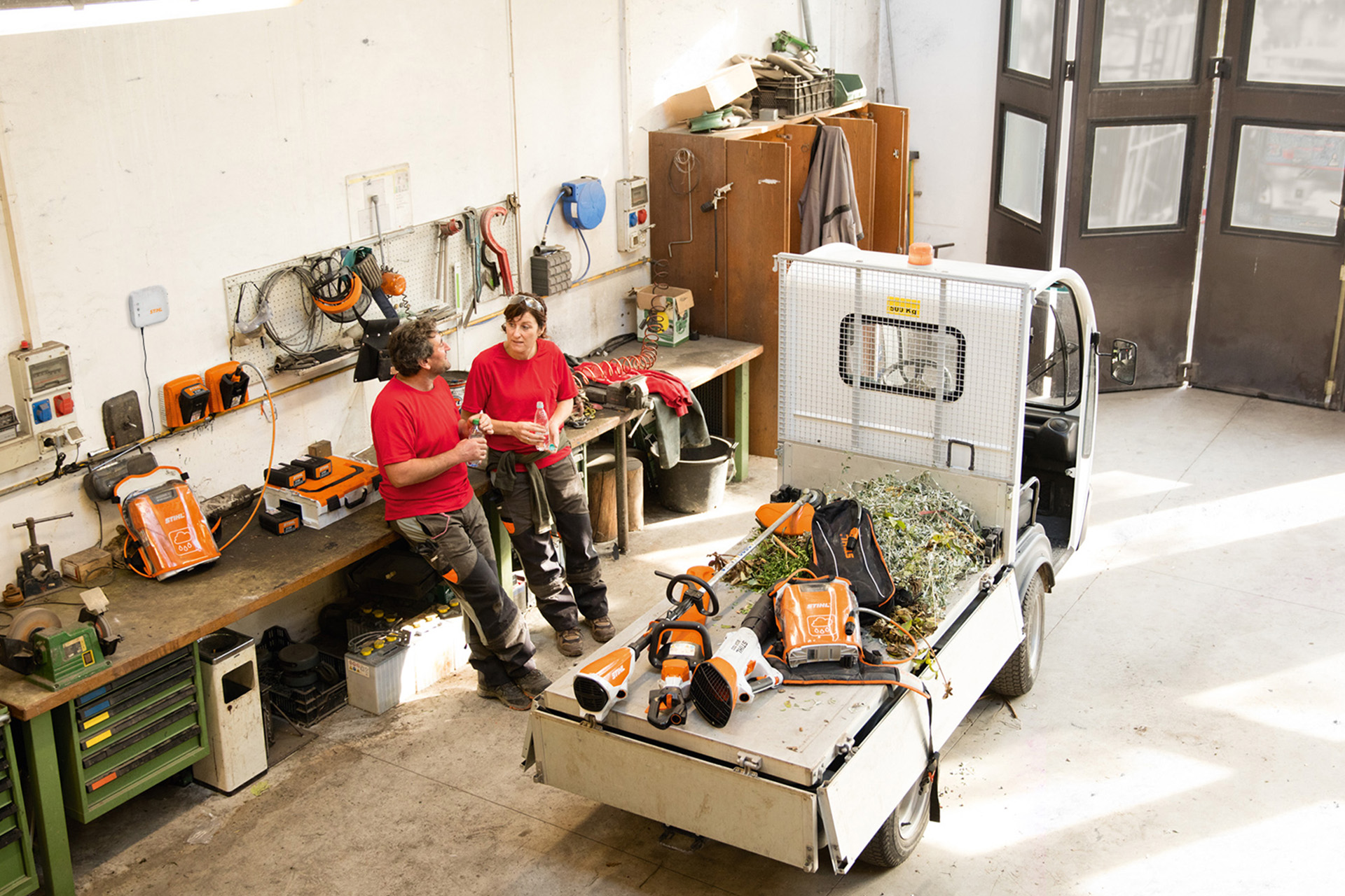 Dos personas hacen una pausa en el taller junto a un camión pequeño con máquinas STIHL en la superficie de carga