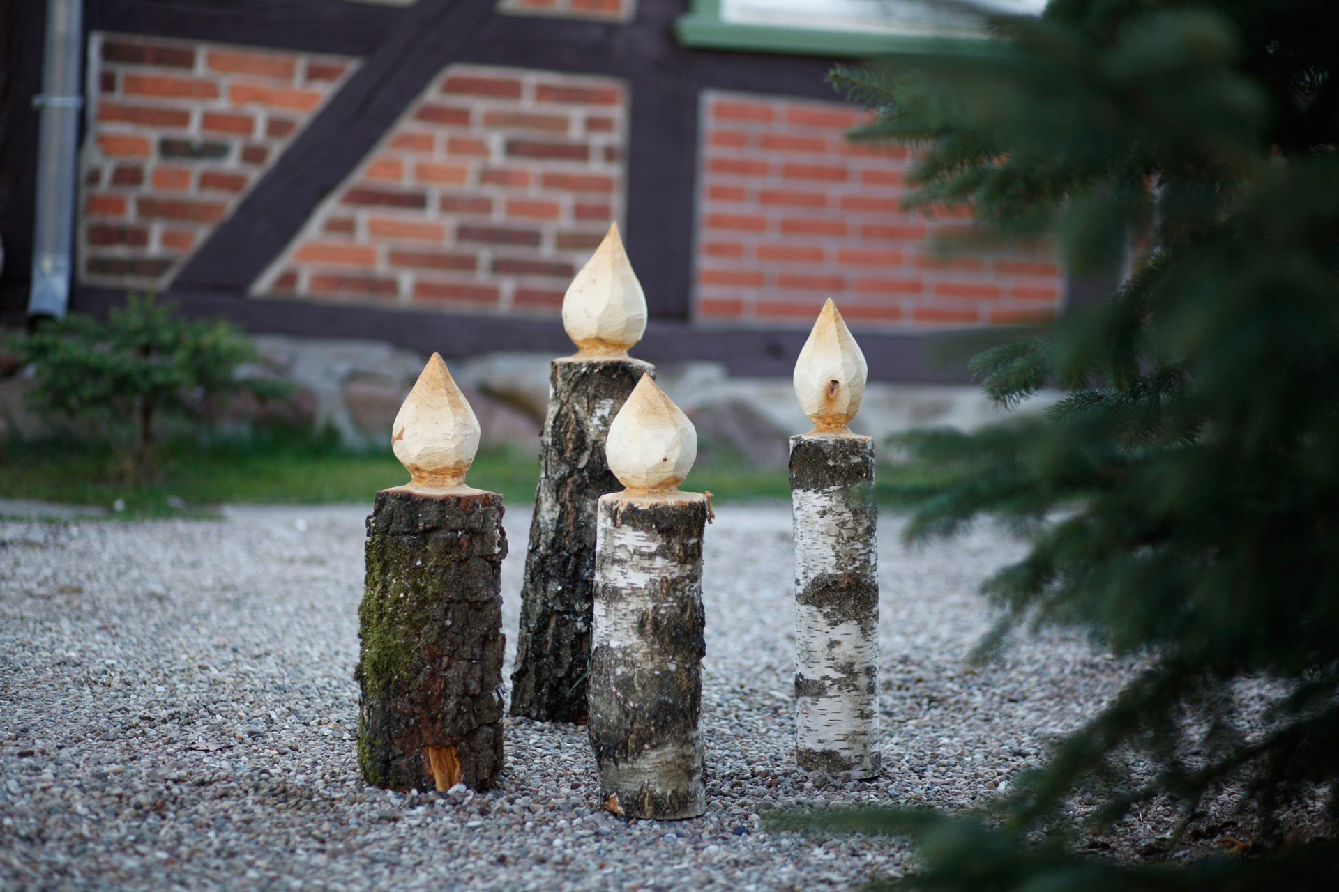 Cuatro velas de madera de pie en un camino junto a un abeto