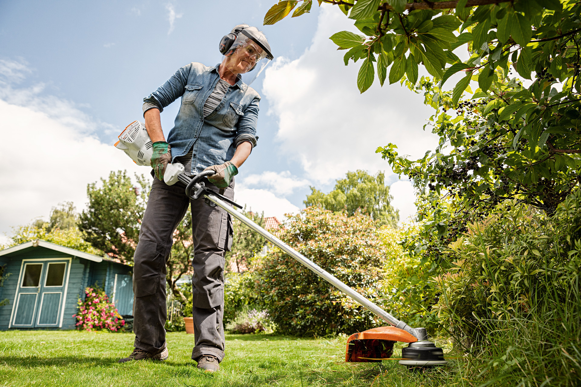 Frau mit Gesichts- und Gehörschutz trimmt Rasen in einem Garten mit der STIHL Benzin-Motorsense FS 56 R