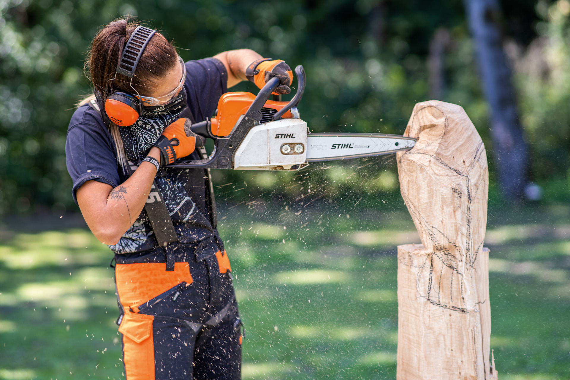 Mujer con equipamiento de protección tallando un búho de madera con una motosierra.