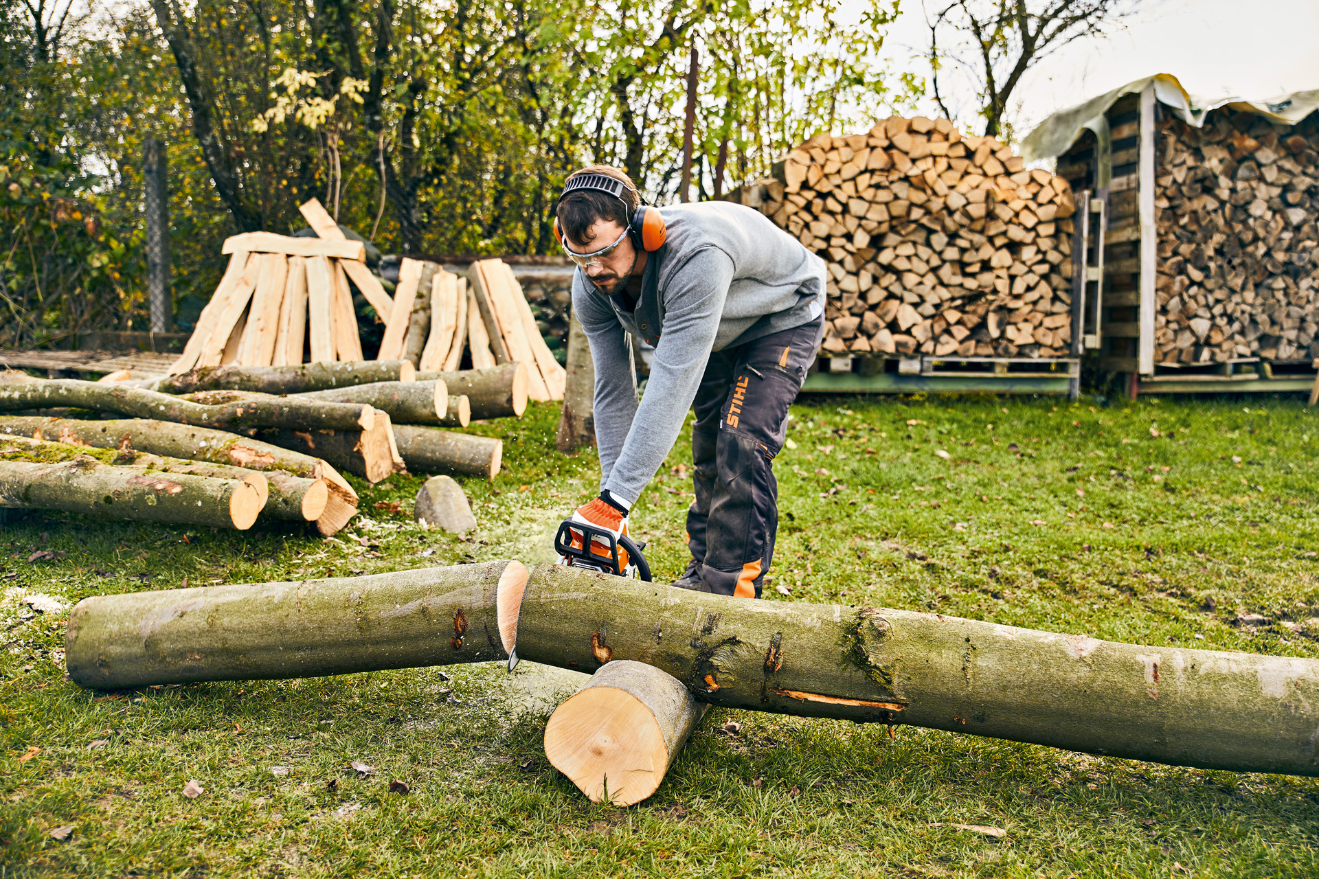 Hombre cortando un tronco de árbol con una motosierra STIHL MS 180 para construir una jardinera de madera artesanal.