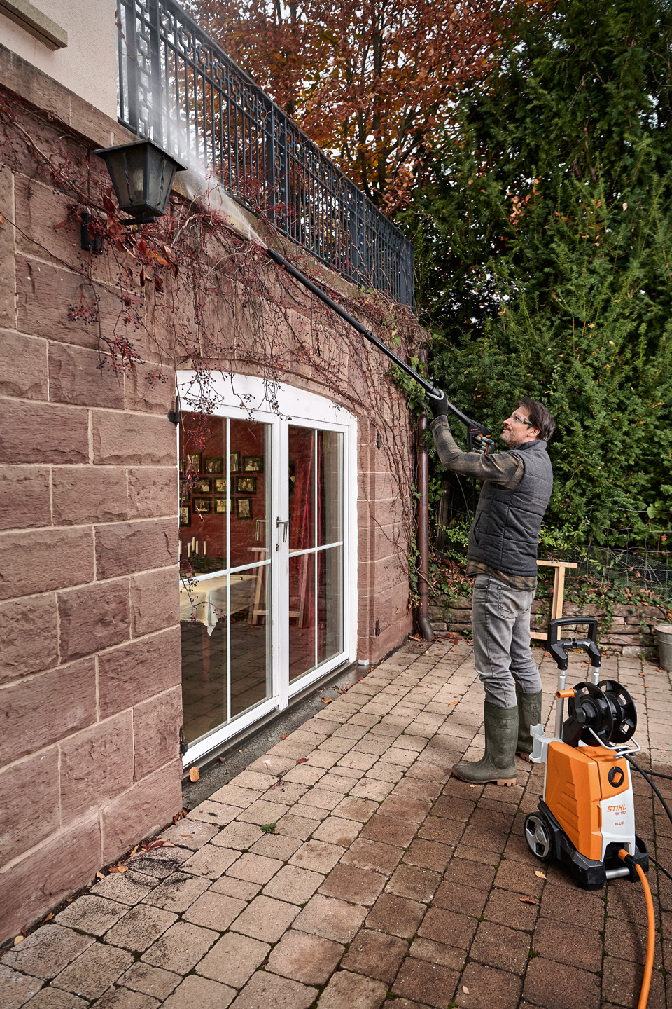 Un hombre de pie en una terraza se encarga de la limpieza de fachadas en una casa con una hidrolimpiadora STIHL