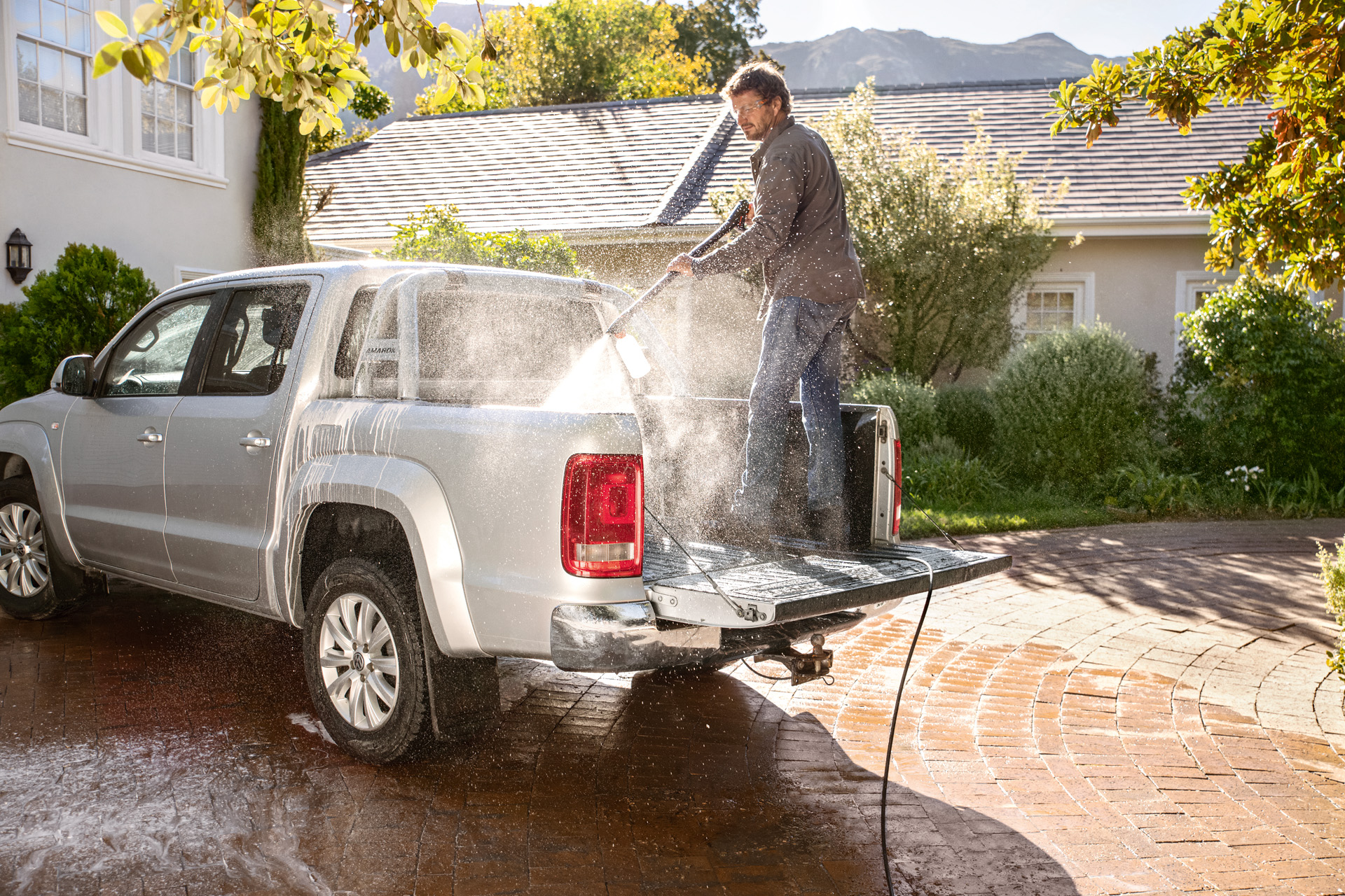 Un hombre de pie en la caja de una furgoneta pick up, sabe cómo lavar un coche con una hidrolimpiadora.
