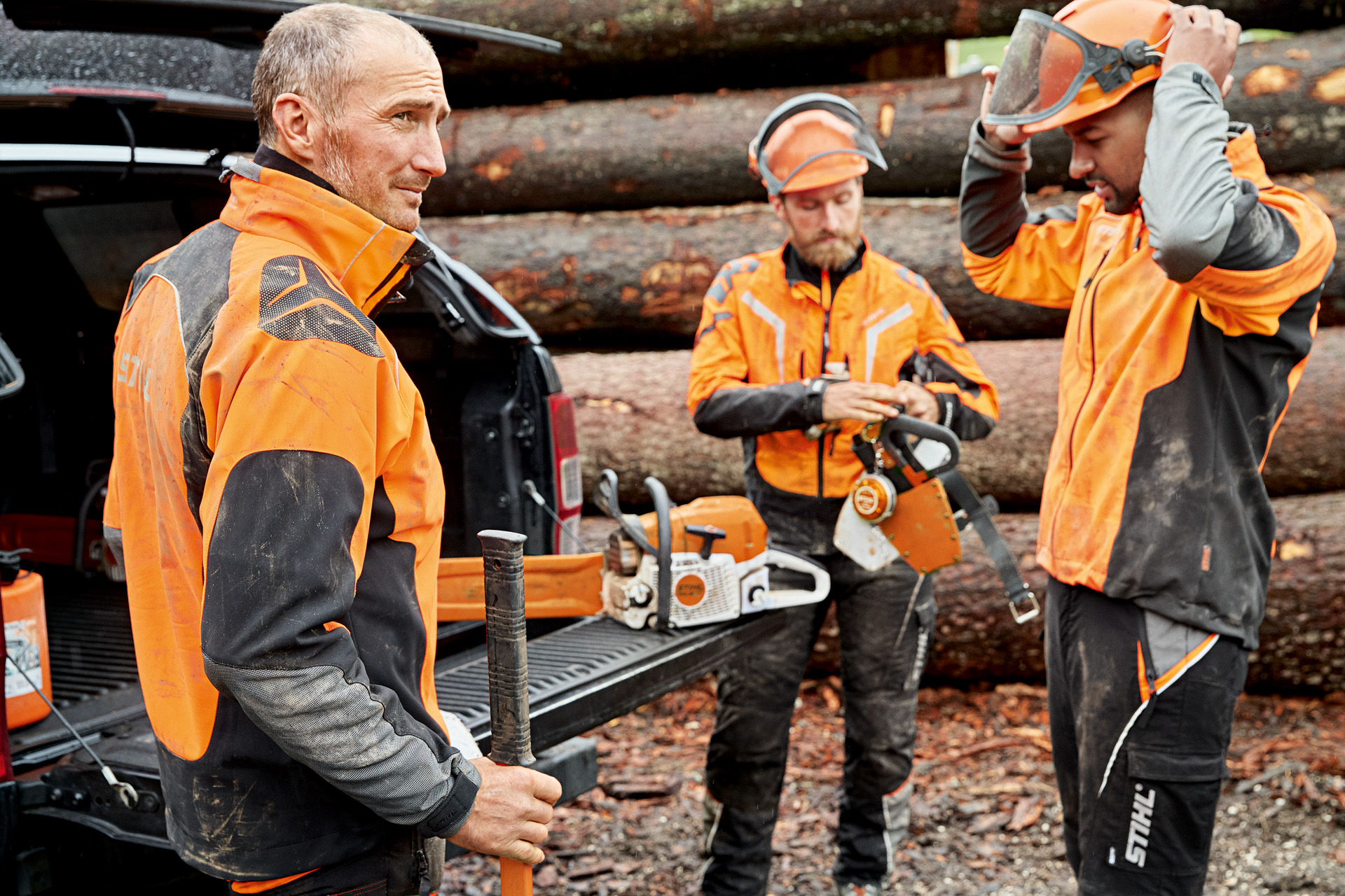 Tres trabajadores forestales con equipamiento de protección individual se preparan delante de unos troncos en el bosque