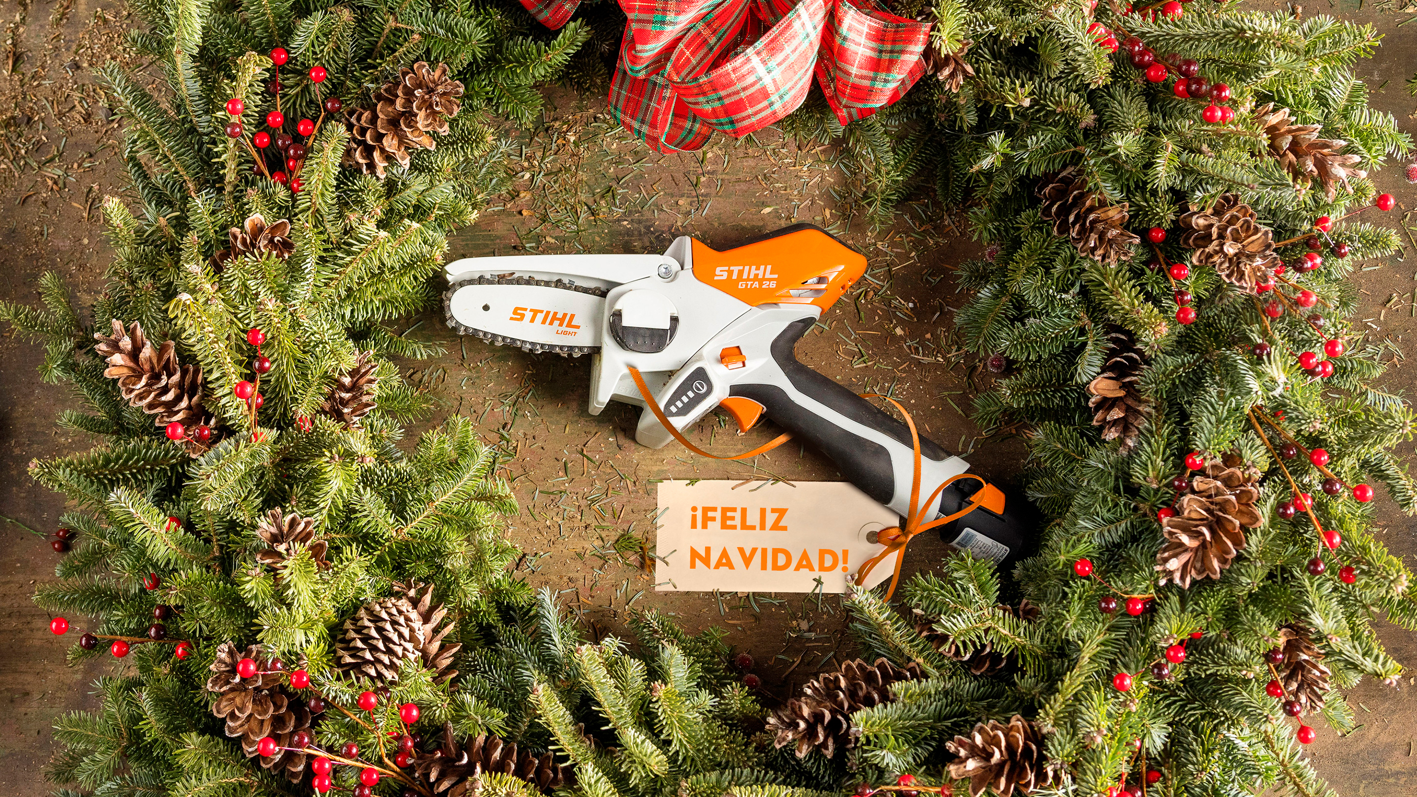STIHL GTA 26 en una corona de Adviento rodeada de hojas verdes de abeto, piñas y una cinta con una tarjeta de Navidad
