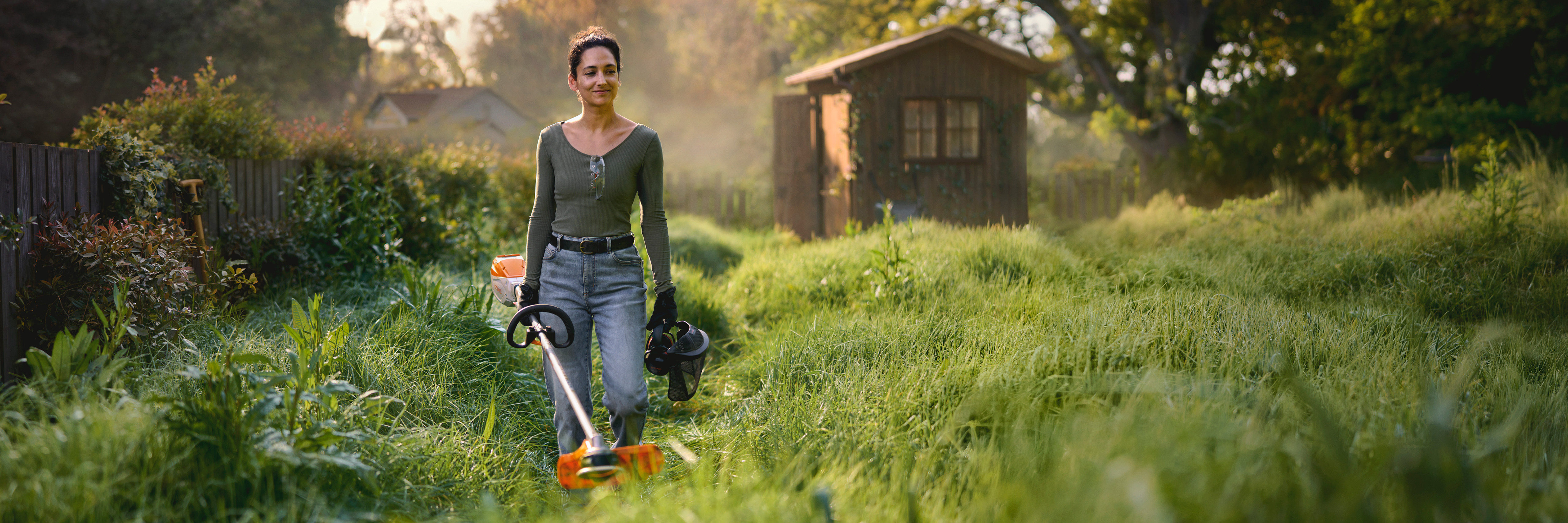 Una mujer andando por un jardín en el que va a trabajar con una desbrozadora de batería STIHL