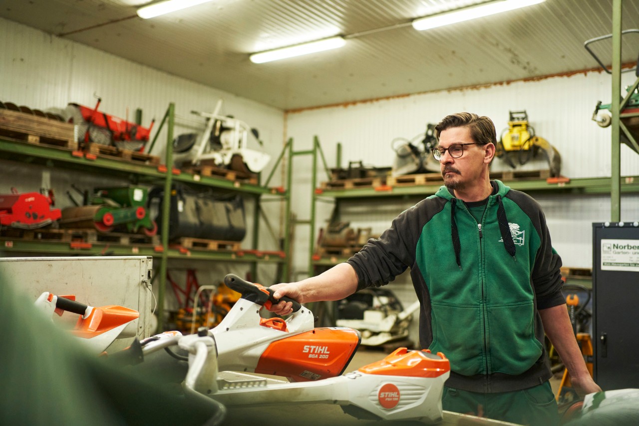 Un hombre en un taller, detrás de una superficie de trabajo con máquinas de batería STIHL, coge el soplador de batería STIHL BGA 200
