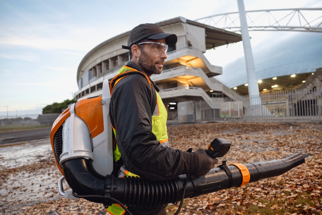 Al anochecer, una persona está limpiando las hojas y los escombros de un estadio con el soplador de hojas inalámbrico ALLPRO STIHL BRA 600.