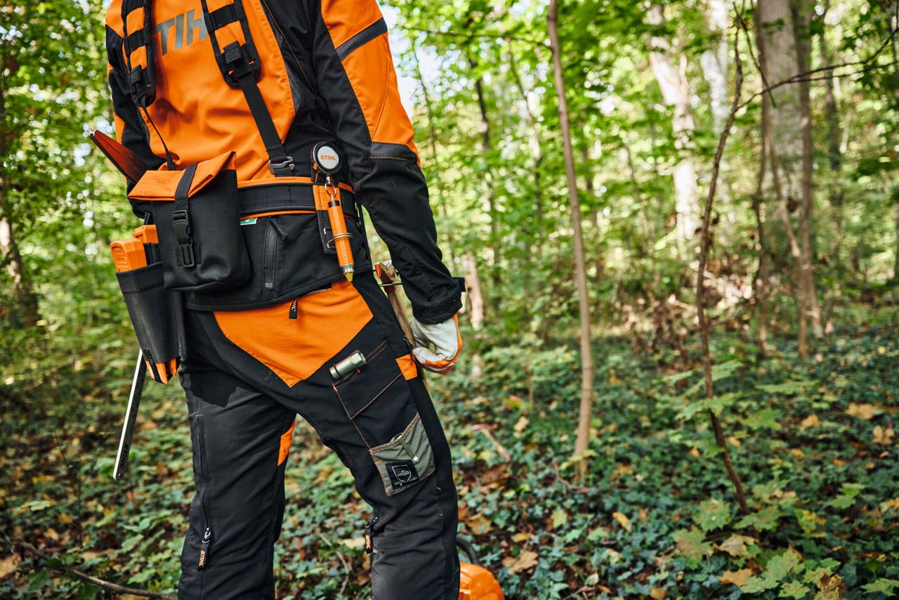 Un hombre trabajando en el bosque con una desbrozadora y llevando el sistema de arnés modular