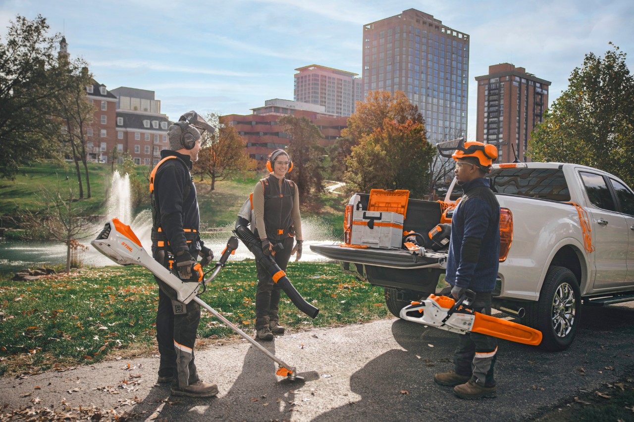 Un grupo de paisajistas profesionales reunidos alrededor de sus vehículos, preparándose para trabajar con herramientas inalámbricas STIHL.