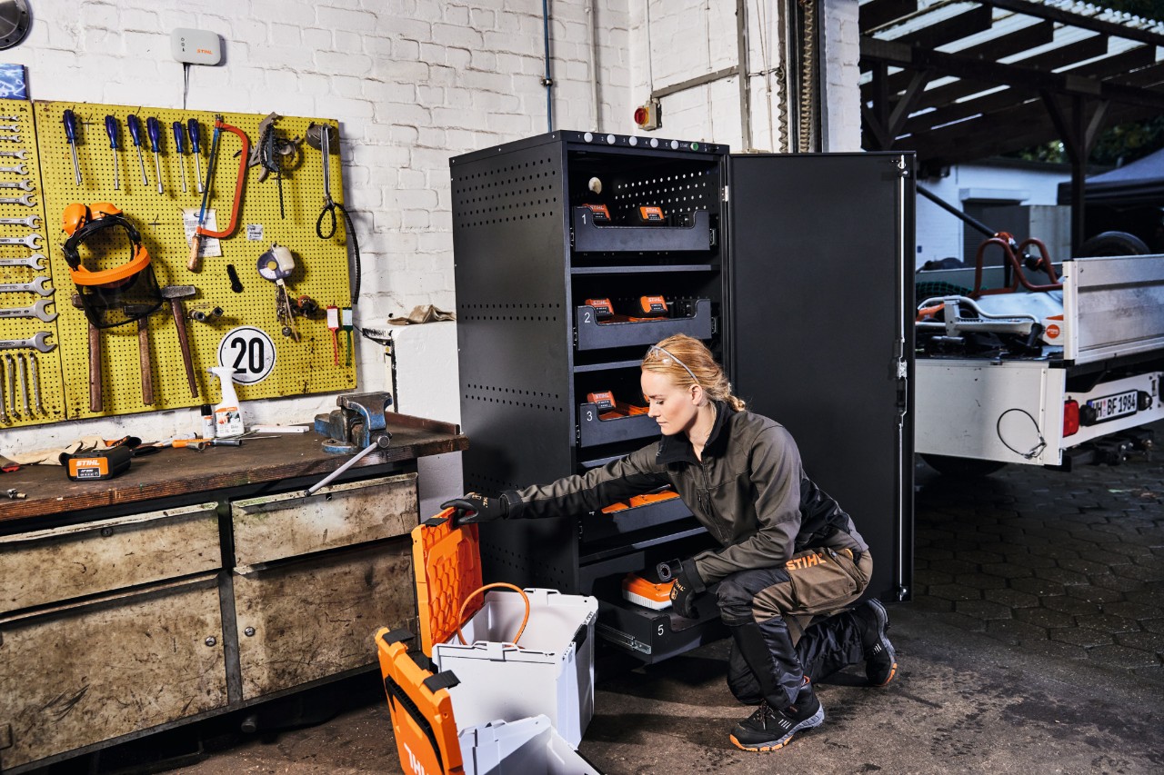 Una mujer con ropa de trabajo en un taller con un armario de carga de baterías y STIHL connected Box.