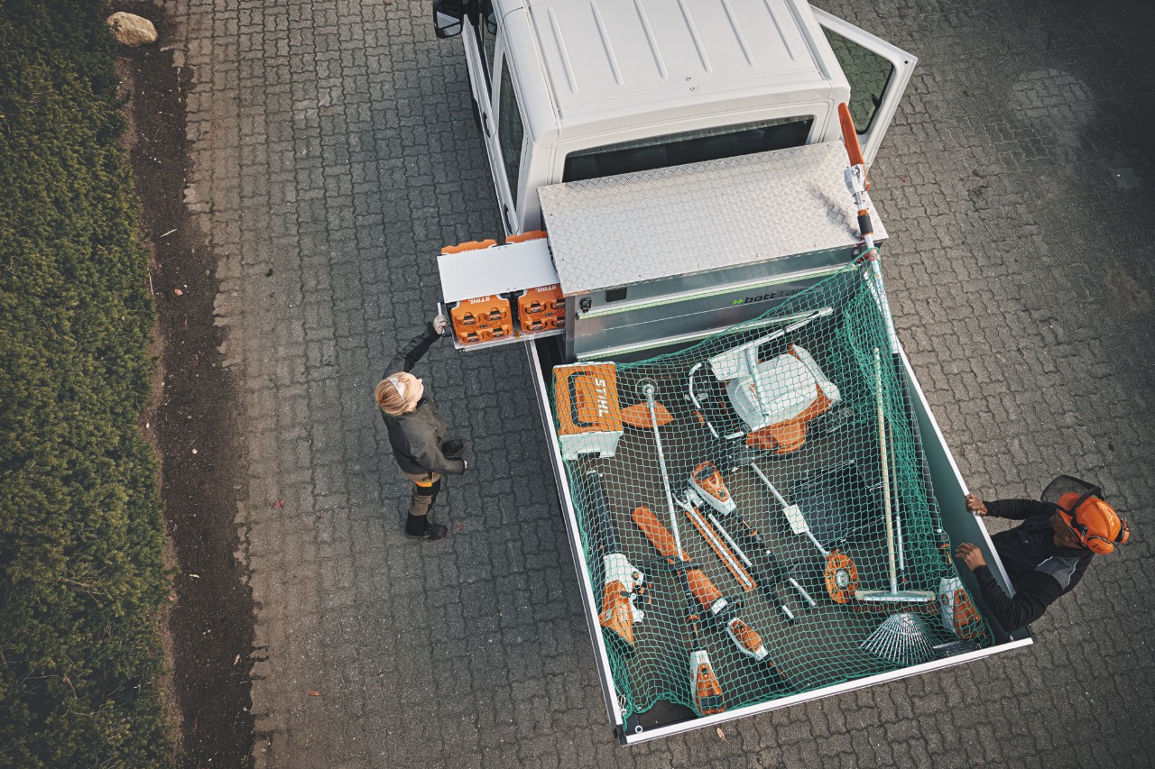Dos profesionales STIHL a vista de pájaro en un vehículo, cargado con el bottTainer y máquinas de batería STIHL.