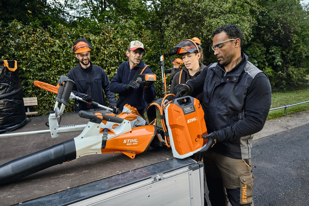 Un equipo de profesionales del paisajismo descarga su equipo profesional a batería STIHL de la zona de carga de un vehículo.